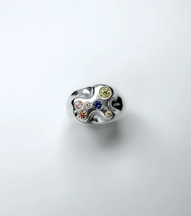 The image is looking down on the face of an organic shaped silver signet ring set with different coloured gemstones on a white background