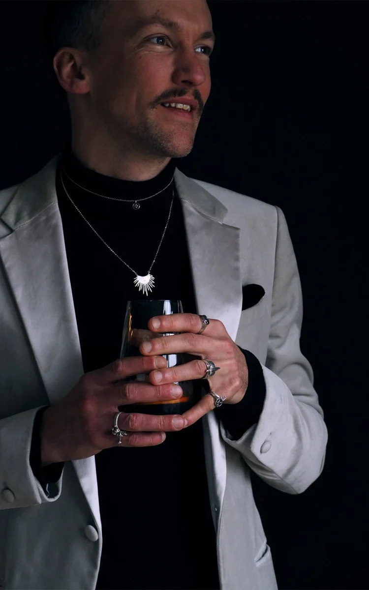 Morano-spiked-halo-necklace-Cheron-mini-skull-medallion-worn-holding-drink-smiling-SLAB-Jewellery.webp