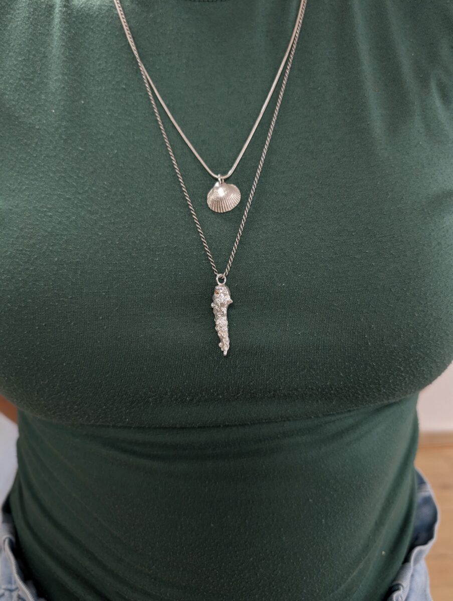 two sea inspired silver necklaces hang against a green top