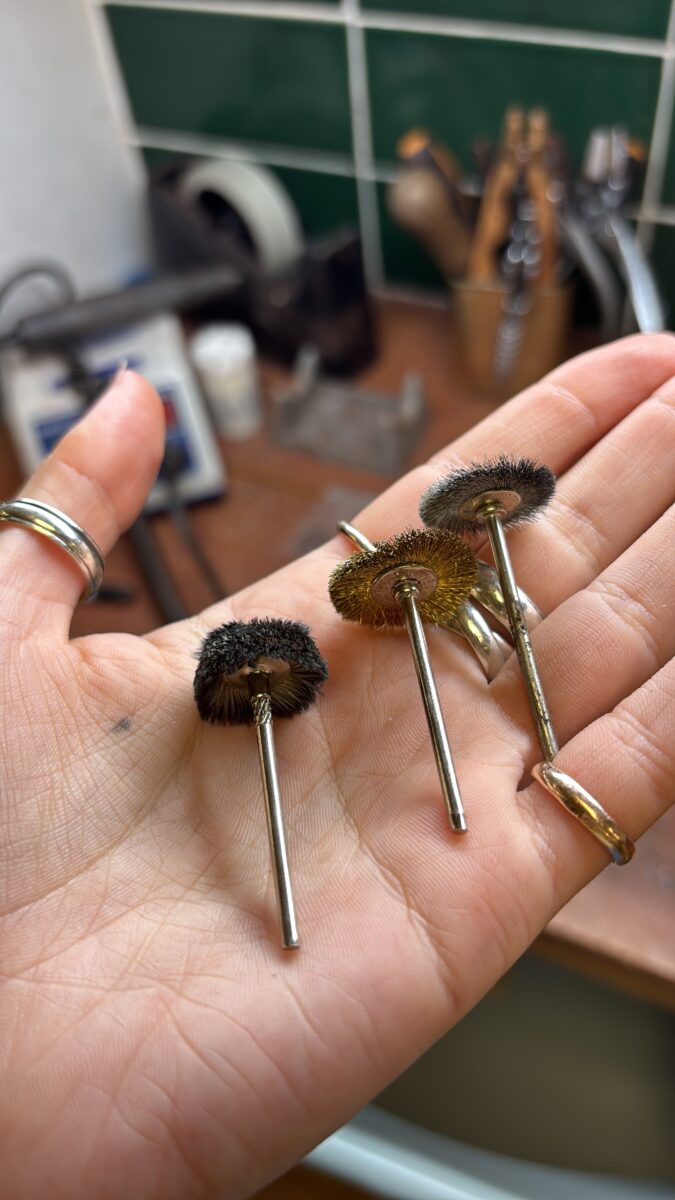Three jewellery finishing brushes rest on a hand ready for polishing
