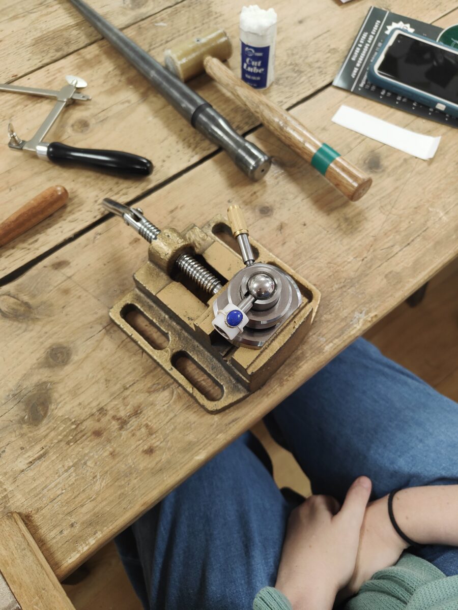 a stone setting vice is set up on a bench with tools. A blue gemstone lapiz lazuli sits ready to be set into silver