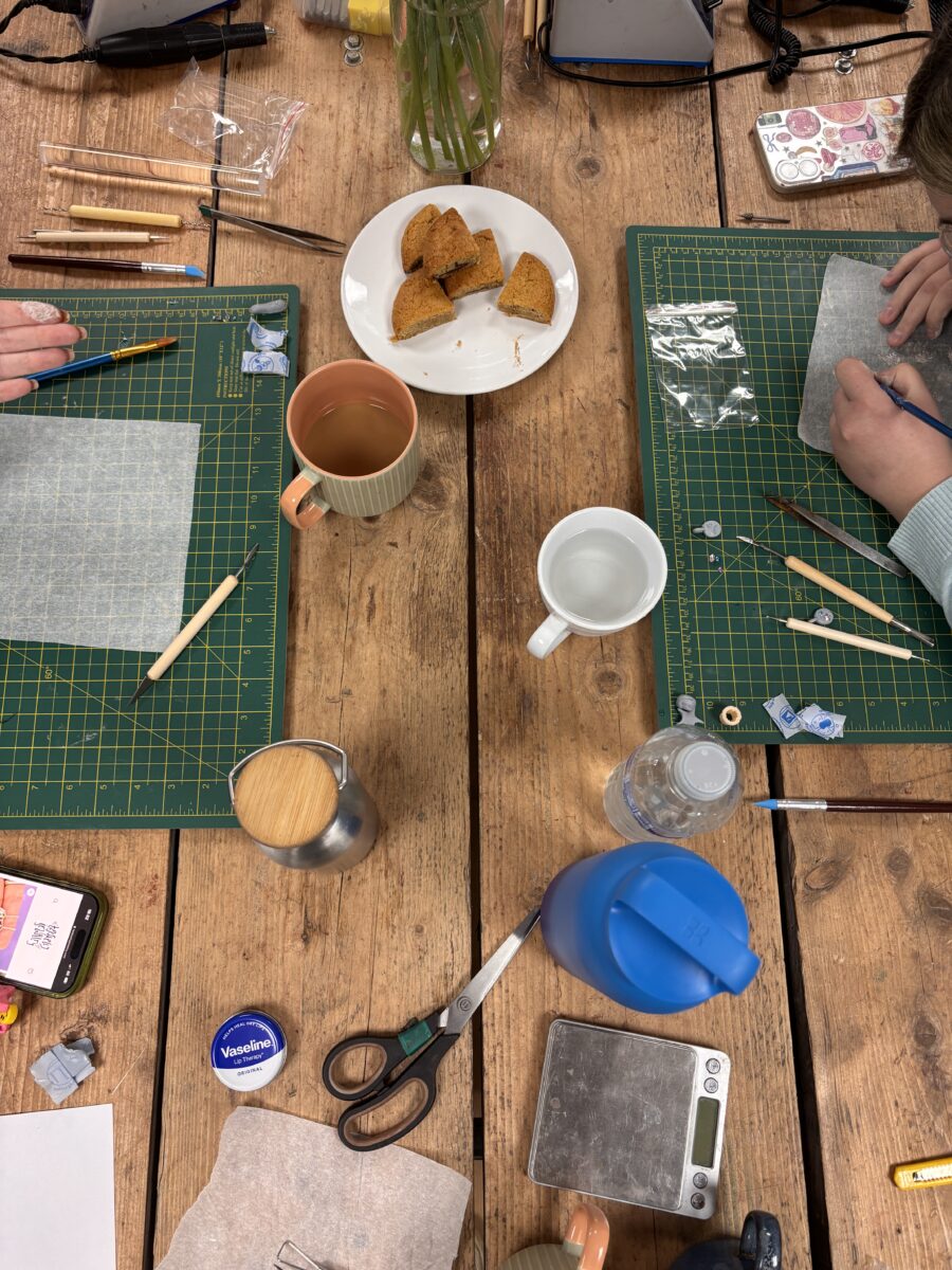 a busy workbench is set with two placces of tools. There are cutting mats, cups of tea and snacks.