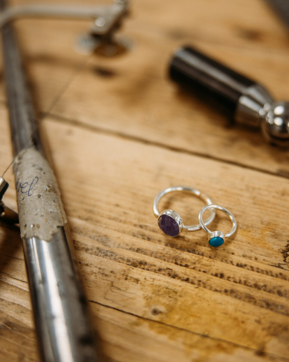 two gemstone rings sit on a worktable surrounded by tools