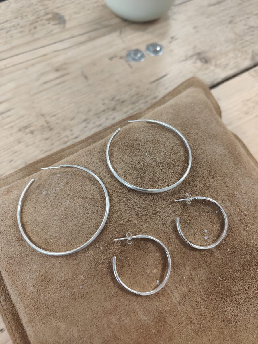 two pairs of handmade silver hoops sit on a brown sandbag