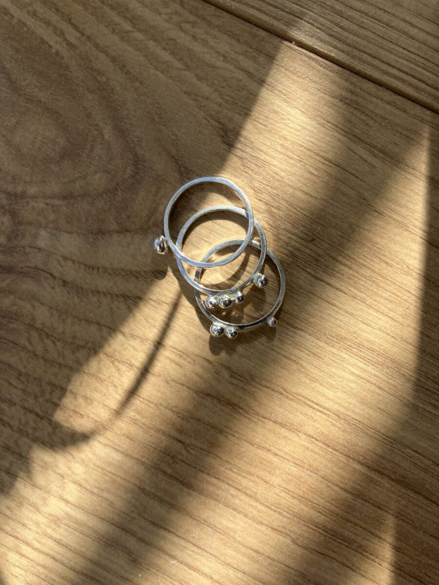 A set of three silver rings with silver ball details of granulation sit on a table in light and shadow