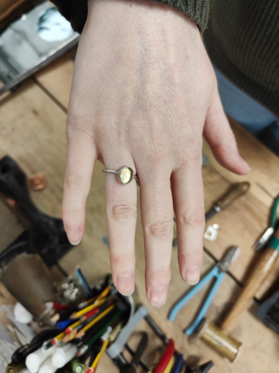 citrine and silver gemstone ring one a hand. In the background are jewellery tools on a workbench