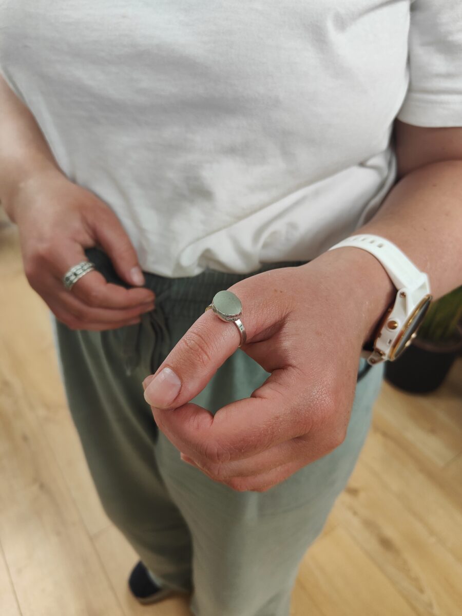 an oval piece of seaglass is set into a silver ring on a hand