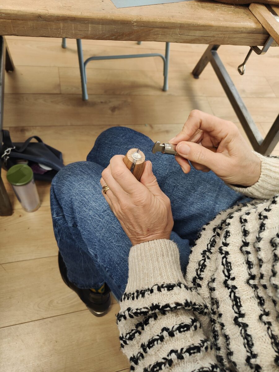 a jewellery workshop participant is holding a ring vice in one hand and a bezel pusher in the other setting a gemstone into a ring