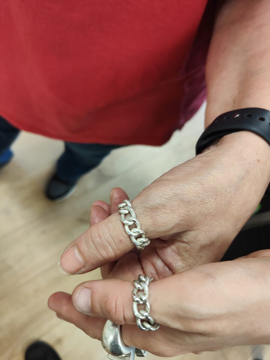 tow thumbs wearing silver curb chain rings. One wrist wears a watch and the person has a red top on
