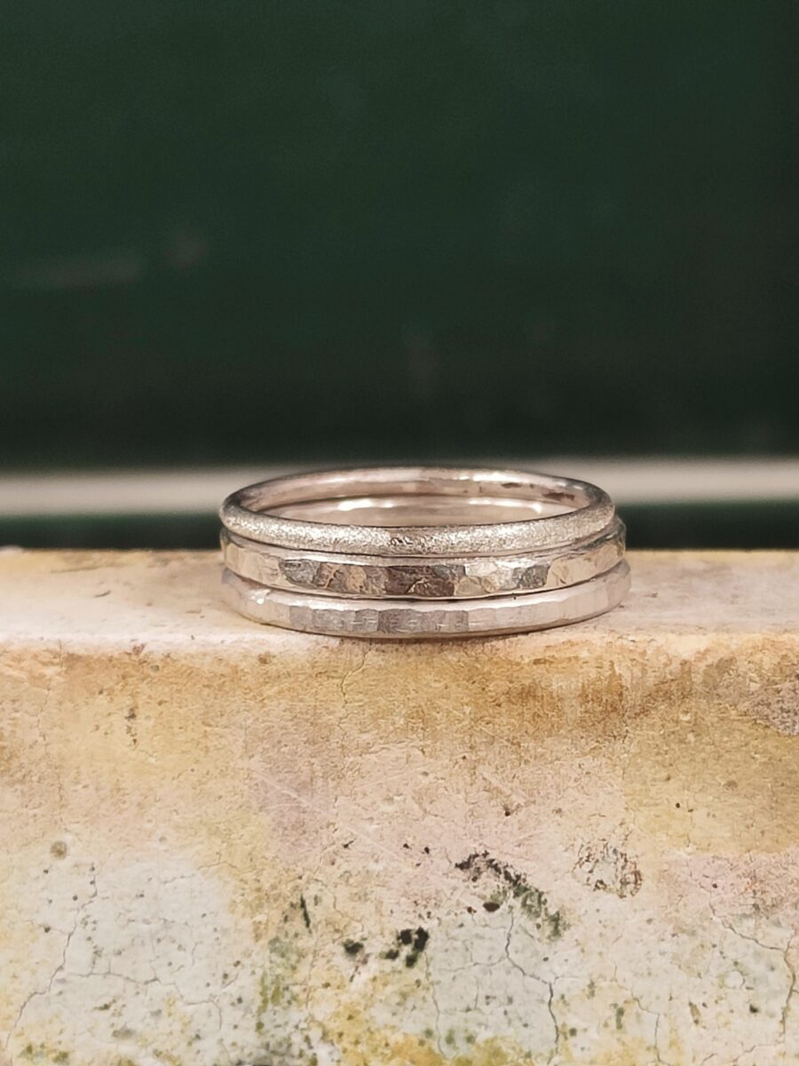 a set of silver stacking rings sit on a textured block with a dark green tile background