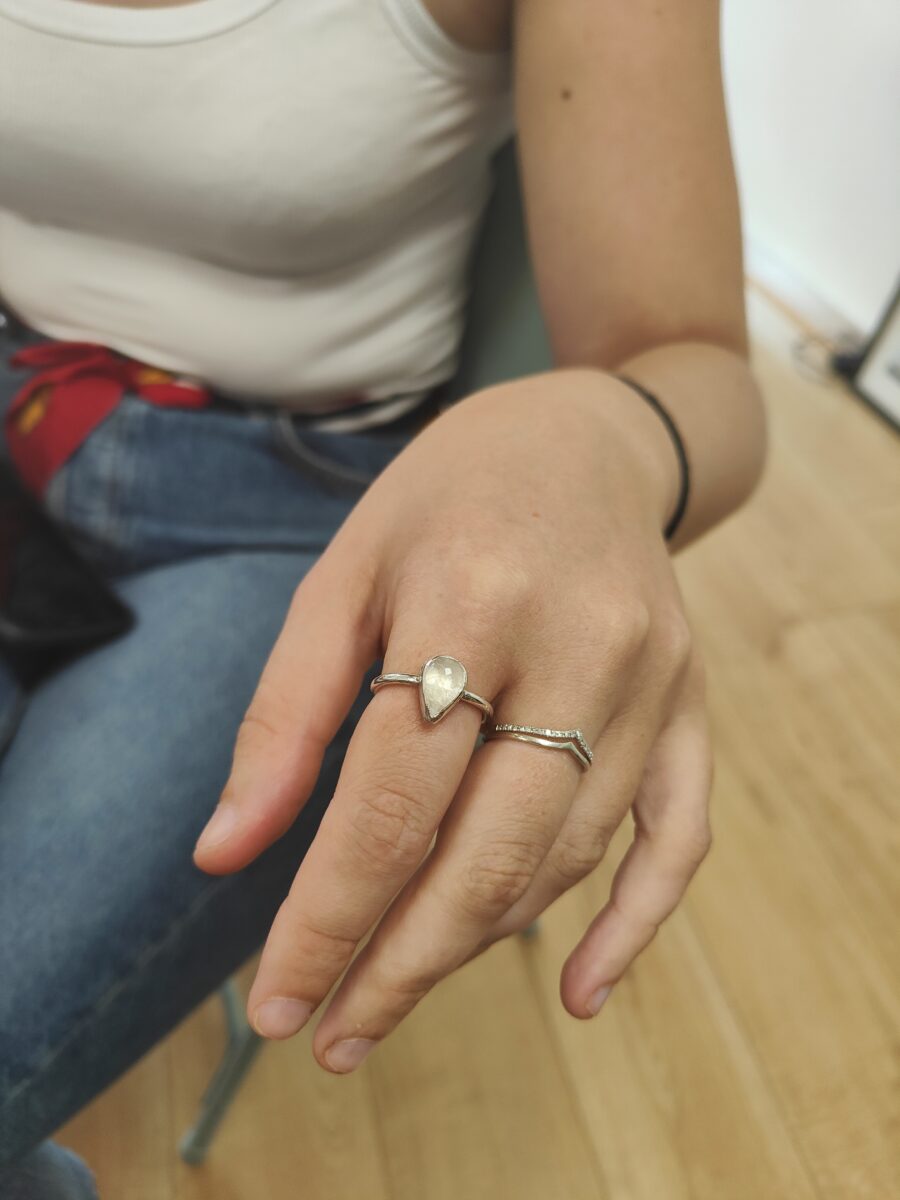 a teardrop moonstone and silver ring sits ona hand with wooden floor behind