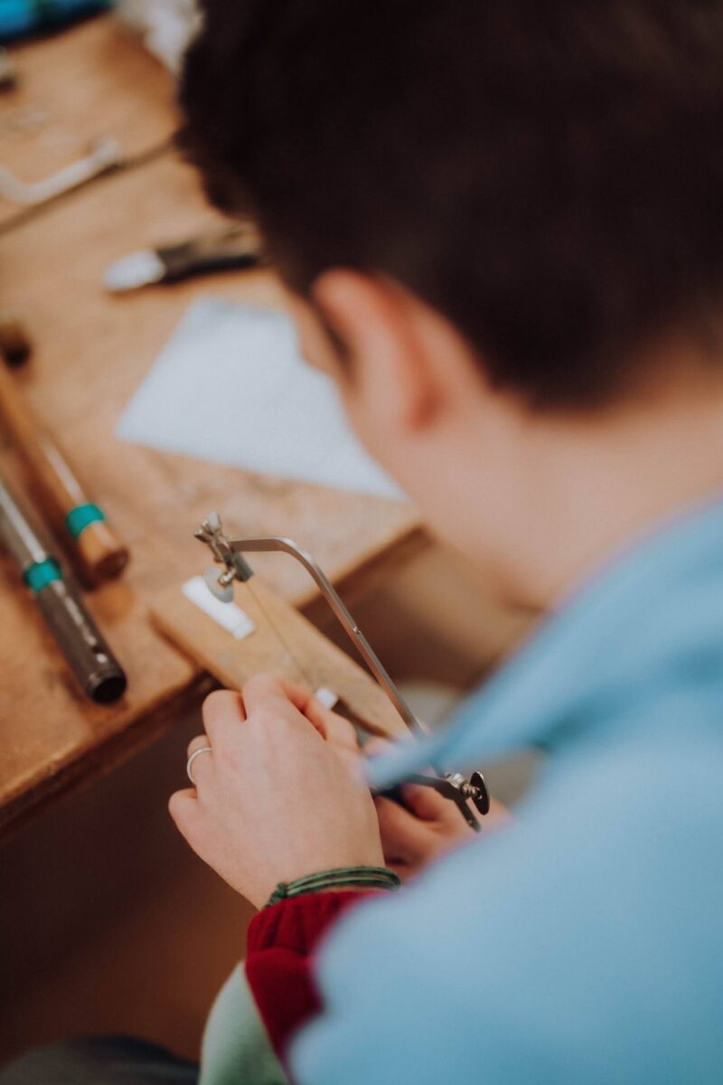 Someone is using a jewellers saw to cut silver while sat at a bench with tools around