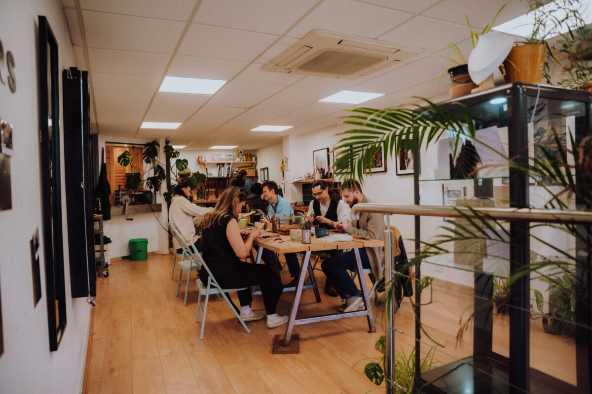 a group of workshop participants sit at a long jewellery bench creating jewellery in a light, airy jewellery studio